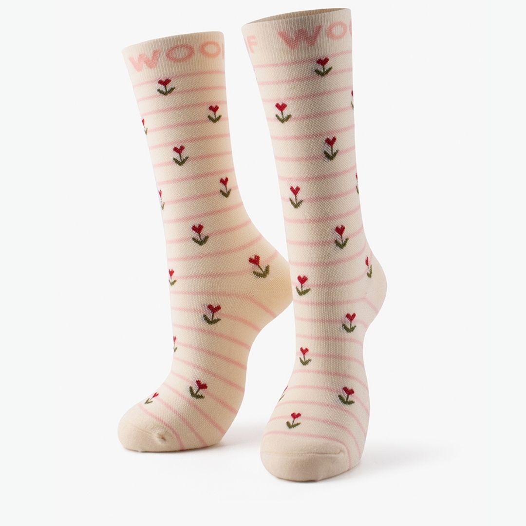 Studio shot of the pair of cream Sweet Buds Bamboo Crew Compression Socks standing upright, featuring thin pink horizontal stripes and micro tulip/flower bud motifs with pink "WOOF" woven into the top cuffs.