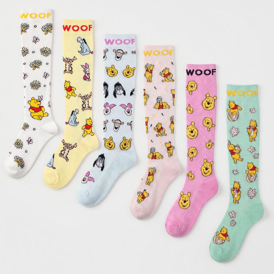 Studio layout displaying the Disney’s Winnie the Pooh Bamboo Compression Socks 6 Pack laid out side by side, featuring six distinct pastels: white floral Pooh print, pale yellow Hundred Acre Wood character print, light blue character face print, soft pink hunny pot Pooh print, vibrant pink repeating Pooh face print, and mint green honey bee Pooh print—each styled with contrast "WOOF" top cuff branding.   